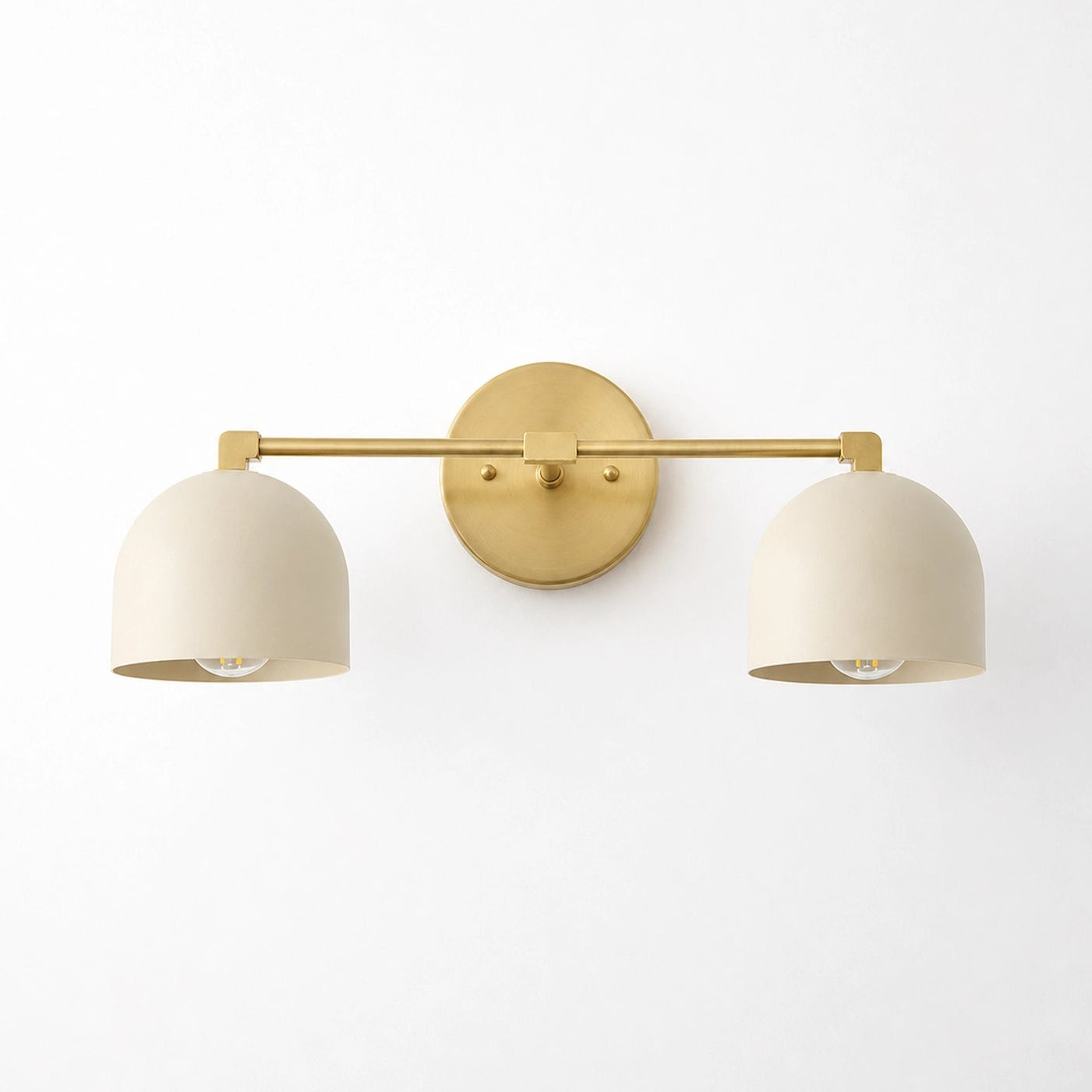 A modern two-light wall sconce with a gold metal bar and circular backplate, paired with two matte cream-colored dome-shaped shades, shown against a plain white wall.