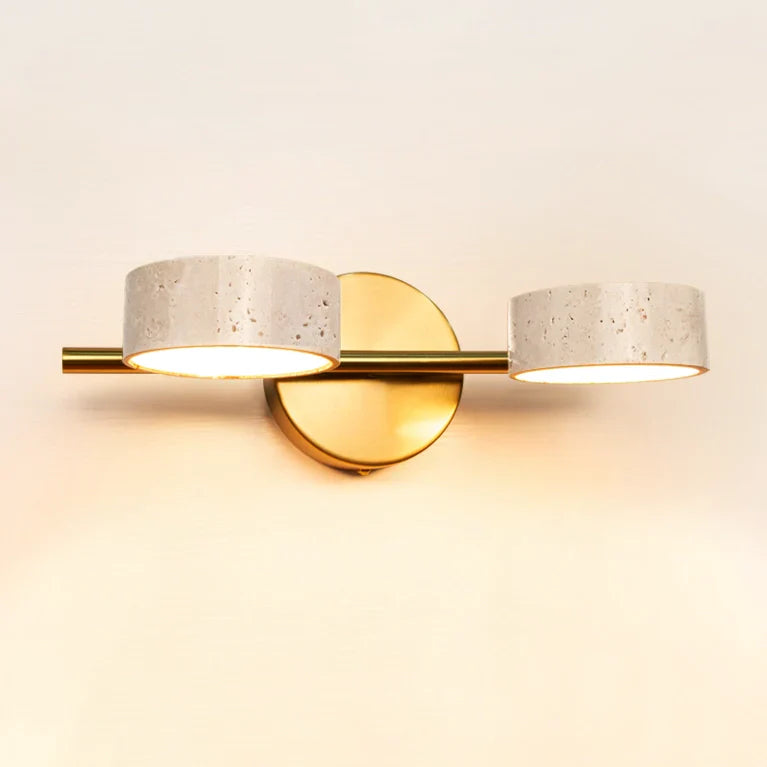 Two-light gold vanity sconce with round travertine shades above a curved bathroom mirror.