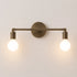 A two-light wall sconce with an antique brass finish and glowing round bulbs, mounted on a plain light beige wall.