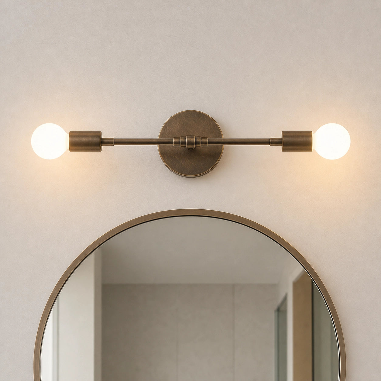 A modern wall-mounted light fixture with two glowing globe bulbs and an oval backplate, installed above a round mirror on a textured beige wall.