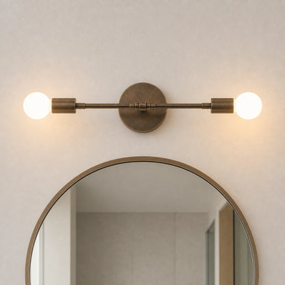 A modern wall-mounted light fixture with two glowing globe bulbs and an oval backplate, installed above a round mirror on a textured beige wall.
