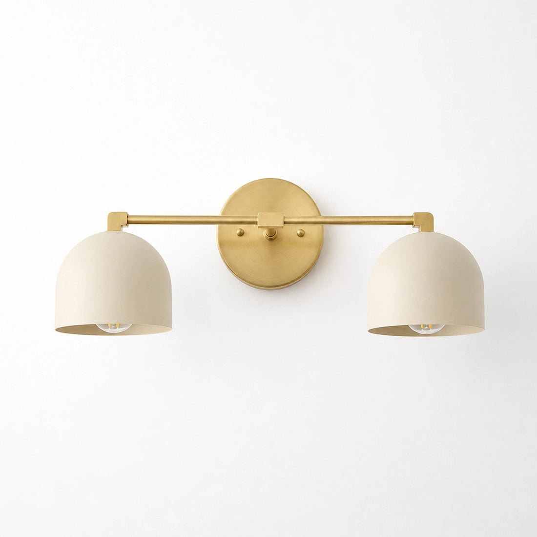 A modern two-light wall sconce with a gold metal bar and circular backplate, paired with two matte cream-colored dome-shaped shades, shown against a plain white wall.