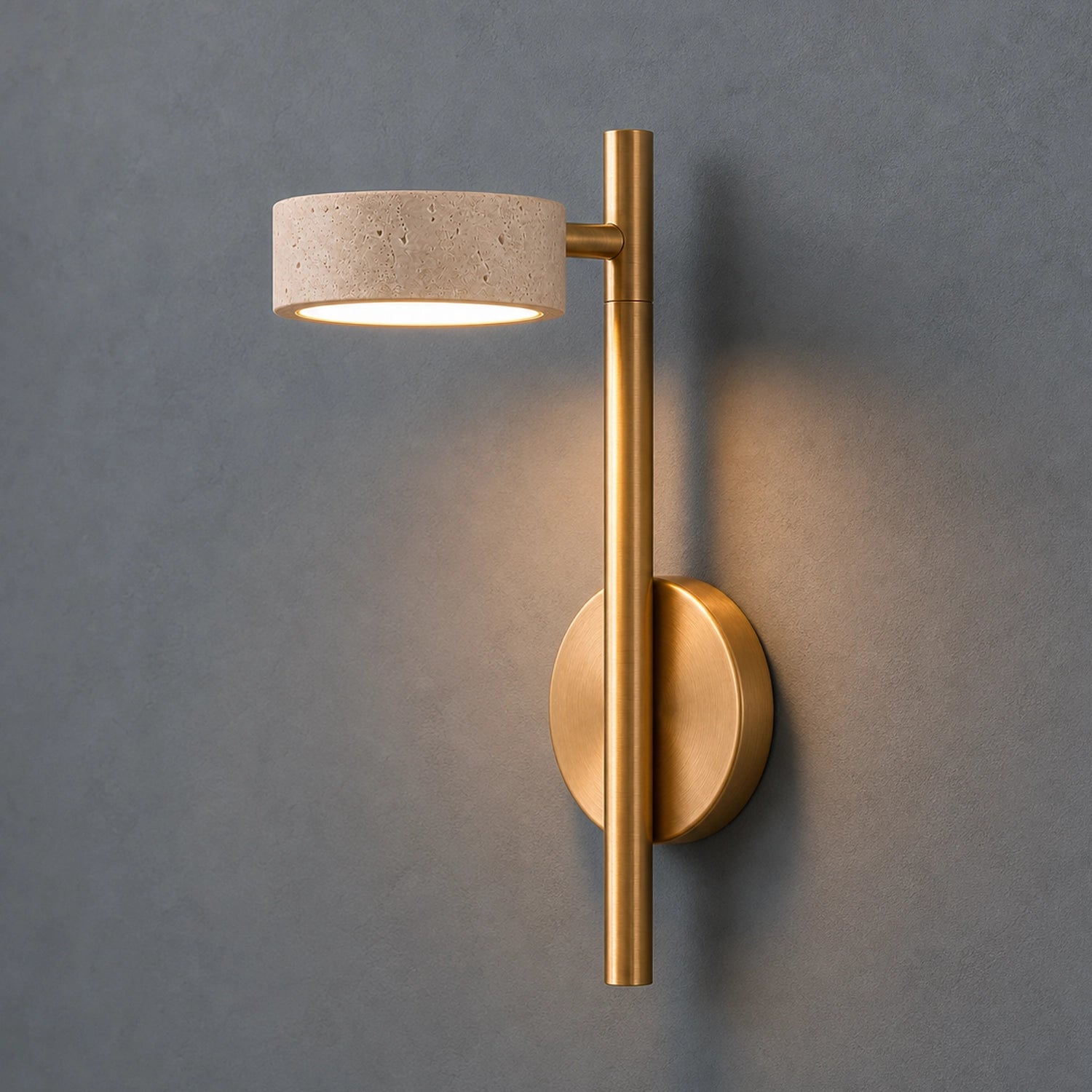 Wall-mounted light fixture with gold finish and travertine shade on a gray background