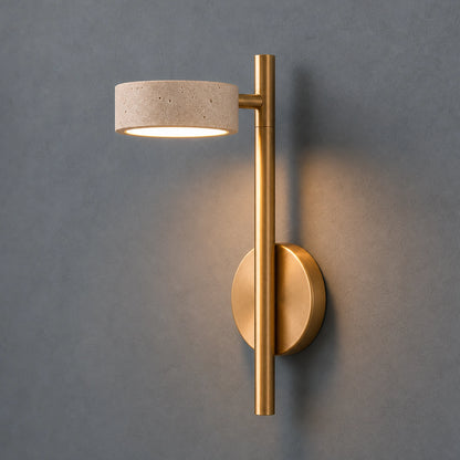 Wall-mounted light fixture with gold finish and travertine shade on a gray background