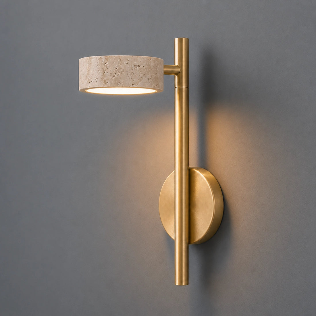 Modern wall sconce with gold finish and travertine shade on a gray wall.