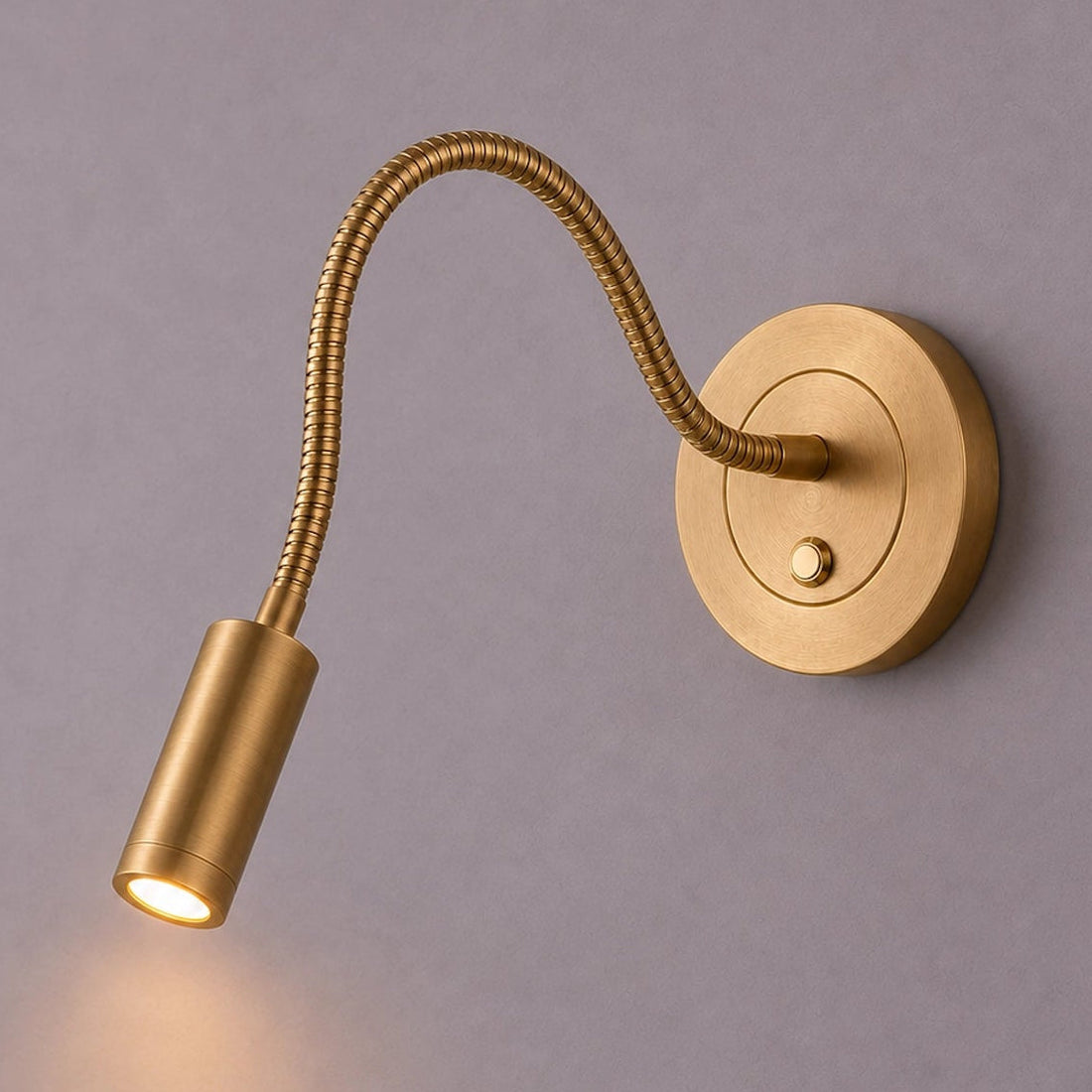 Gold wall-mounted reading light with flexible arm on a gray background