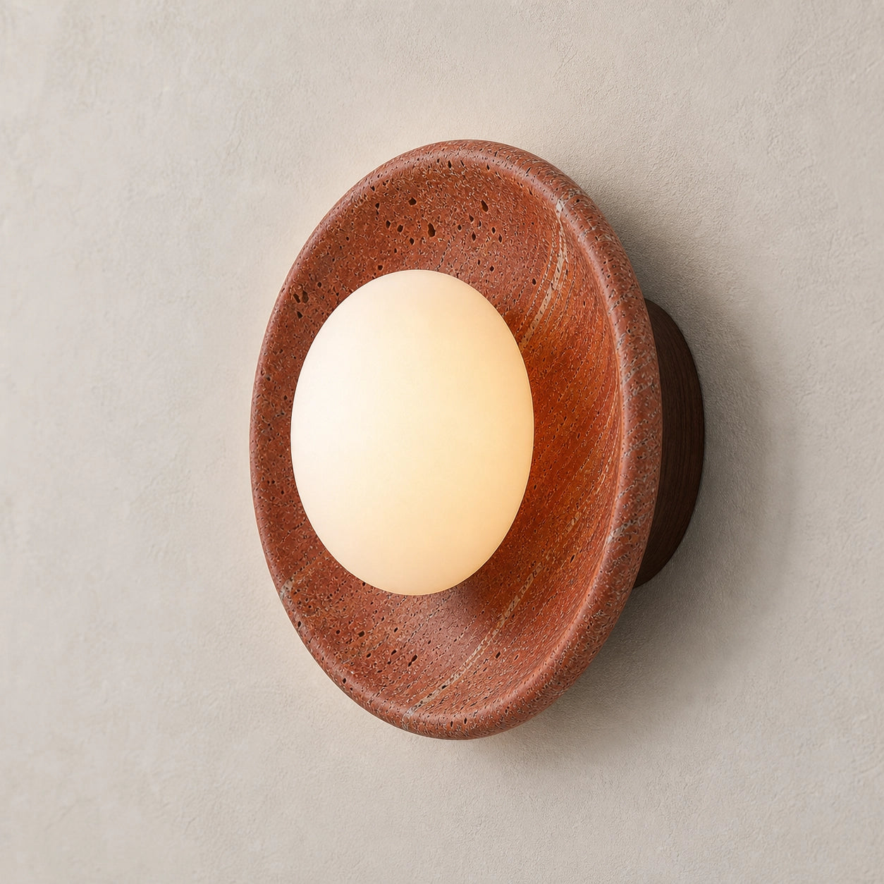 Red travertine round wall sconce with a globe glass shade on a beige background