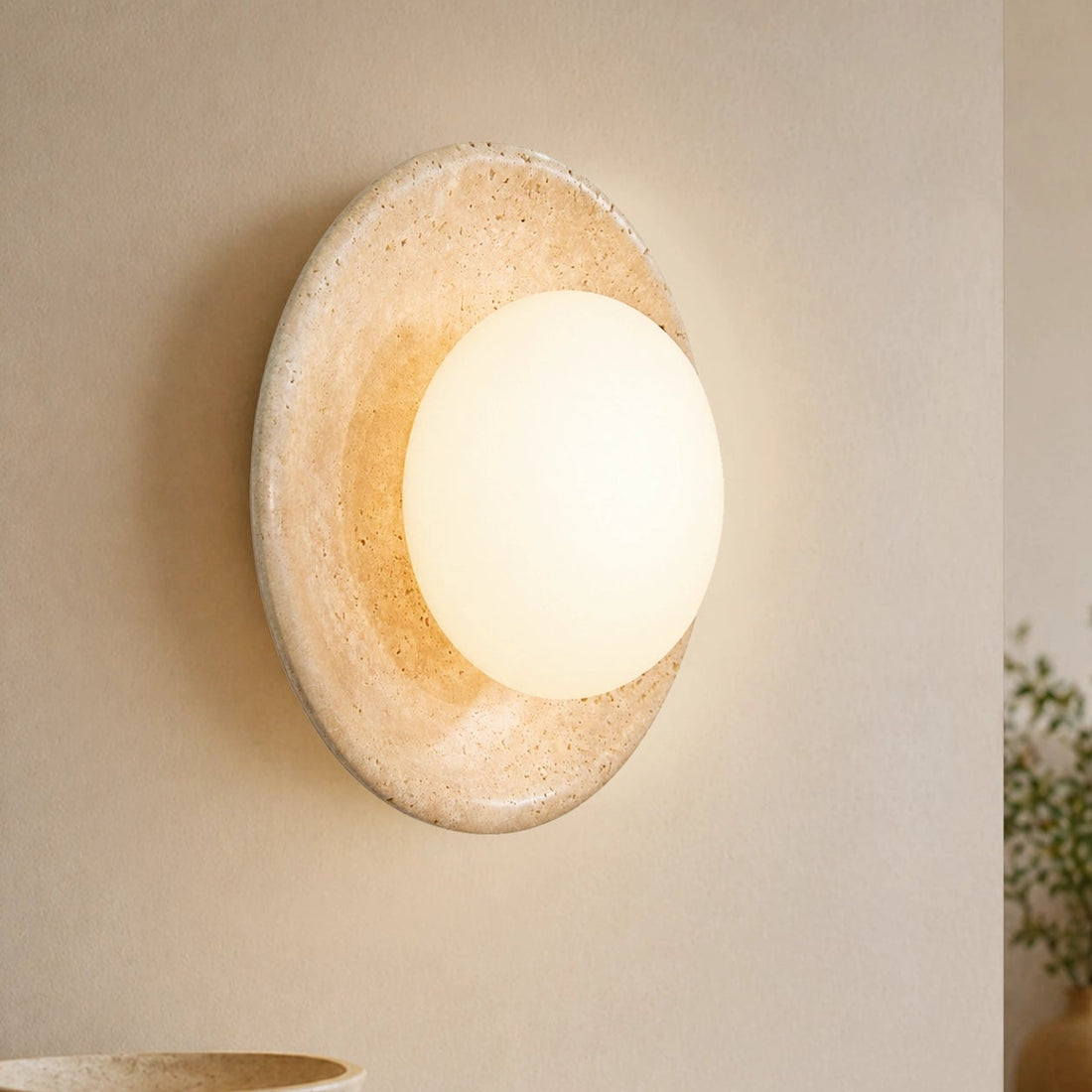 Round travertine wall light fixture on a beige wall with a cozy indoor setting.