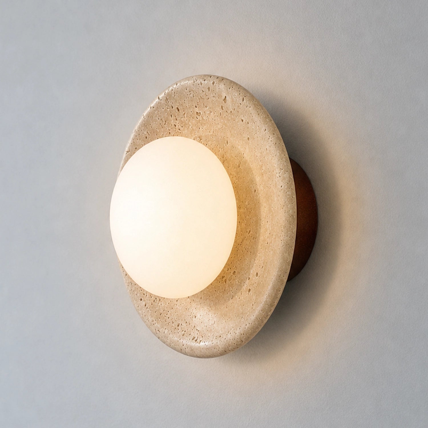 Round travertine wall sconce with a globe glass shade on a neutral background