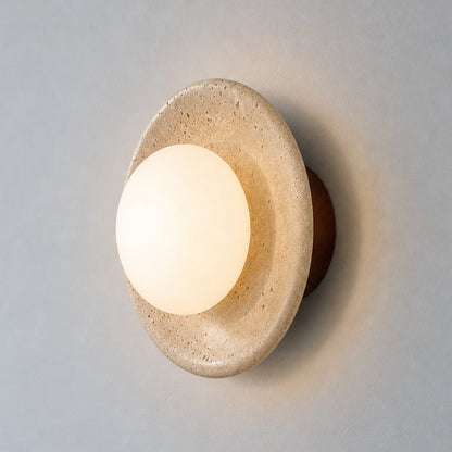 Round travertine wall sconce with a globe glass shade on a neutral background