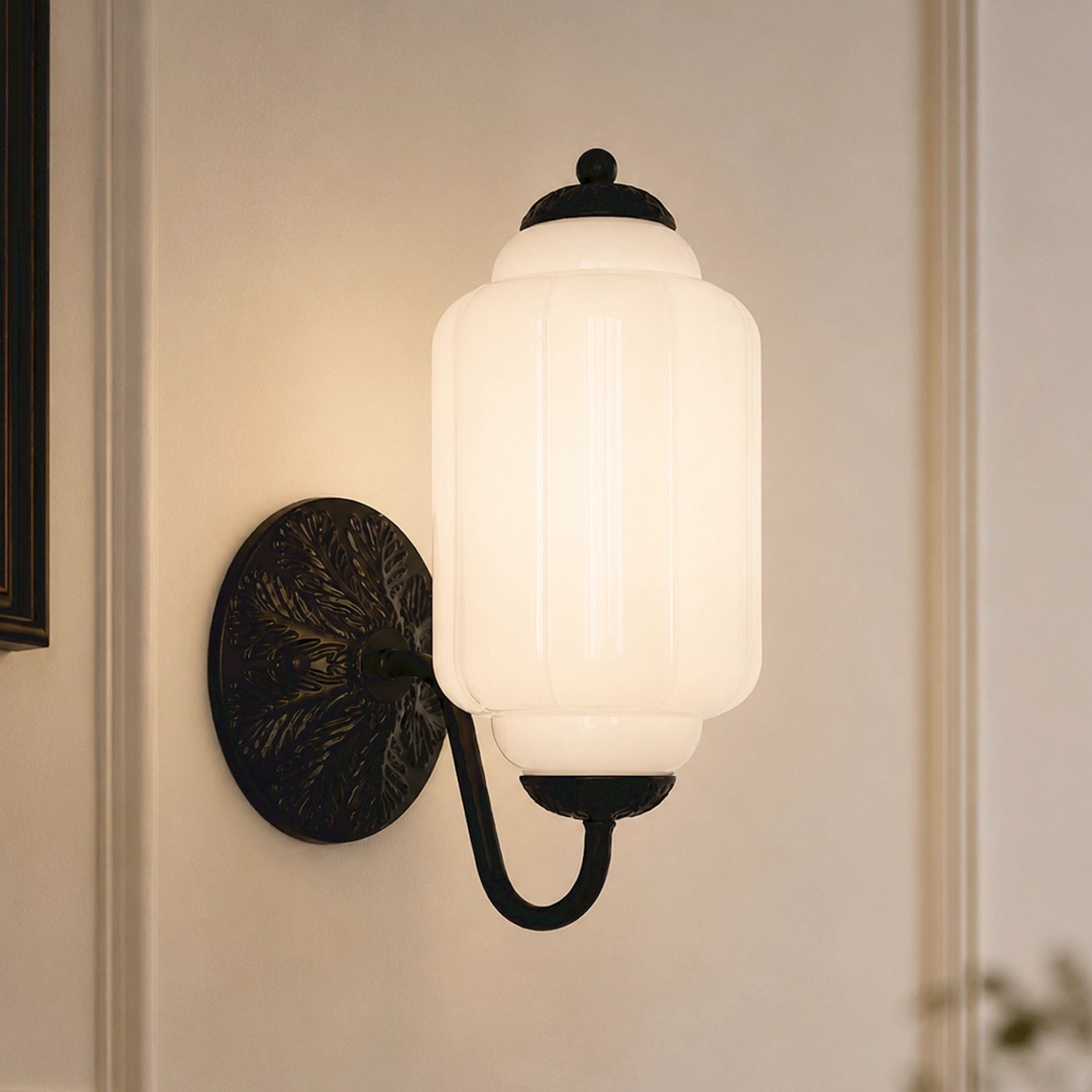 Wall-mounted light fixture with white eloise glass shade and black metal fixture on a neutral wall.