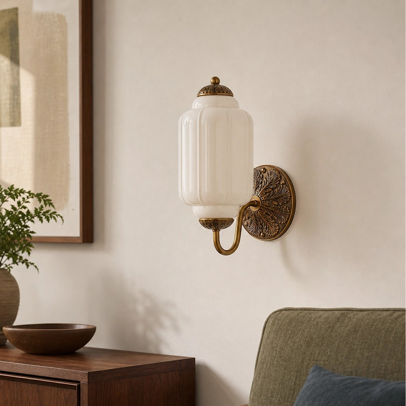 White eloise glass wall sconce on a wall with a plant and wooden cabinet in the foreground